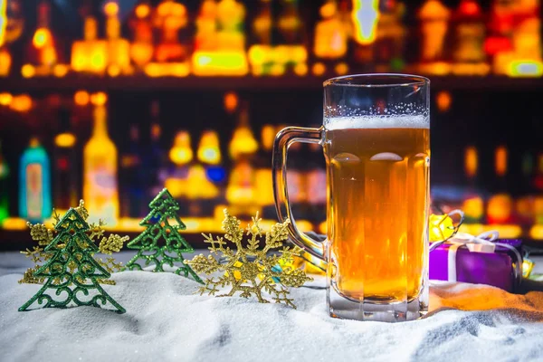 Mug of beer with Christmas decoration. Glass of light beer with foam in snow with creative New Year holiday artwork. Copy space