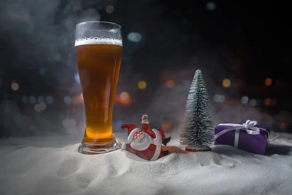 Mug of beer with Christmas decoration. Glass of light beer with foam in snow with creative New Year holiday artwork. Copy space