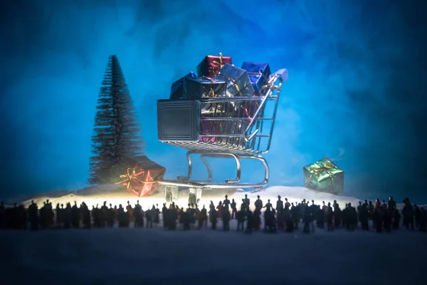 New year or Christmas holiday shopping concept. Store promotions. Silhouette of a large crowd of people watching at a big shopping trolley with gifts. People on snow ready to shopping. Selective focus