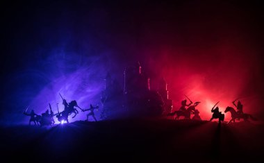 Süvari ve piyadelerle ortaçağ savaş sahnesi. Şekillerin siluetleri ayrı nesneler olarak, karanlık tonlu sisli arka planda ortaçağ şatosuyla savaşan savaşçılar arasında. Seçici odak