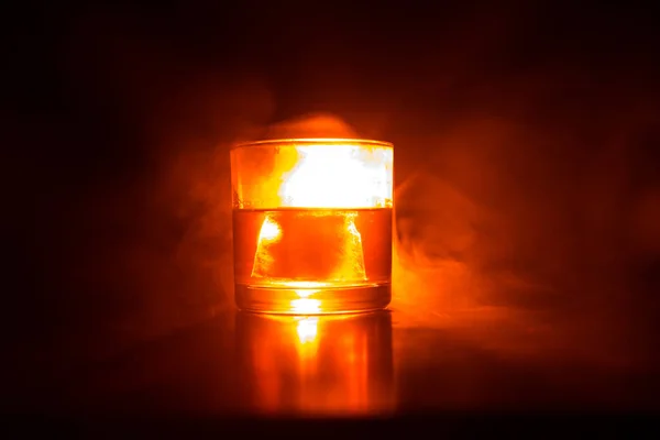 威士忌在火概念 玻璃杯的威士忌和冰在木表面上的彩色光和雾的背景 关门了选择性聚焦 — 图库照片