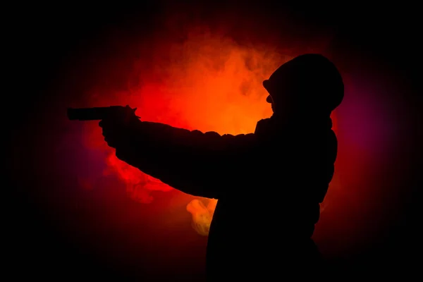 Silhouette of man with pistol ready to attack on dark toned foggy background or dangerous bandit holding gun in hand. Shooting terrorist with weapon theme decor