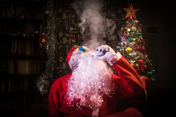 圣诞老人在黑暗的背景下 用蒸汽云 以传统圣诞老人的服装 用电子香烟 选择性对焦 在背面的冷杉树 — 图库照片