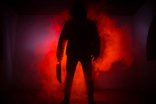 Опасный человек в капюшоне, стоящий в темноте и держащий нож. Лицо не видно. Совершение преступления
