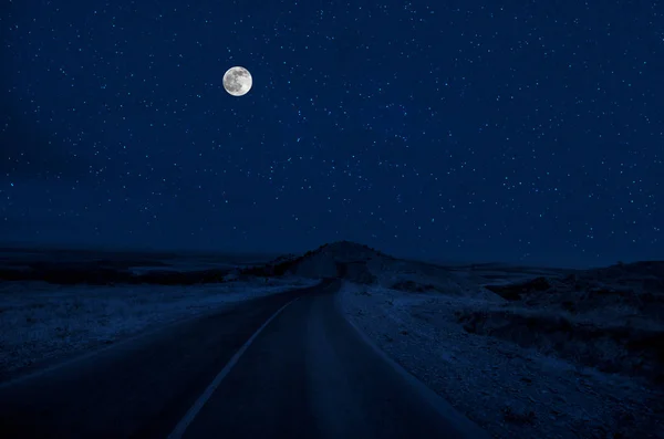 Mountain Road through the forest on a full moon night. Scenic night landscape of country road at night with large moon