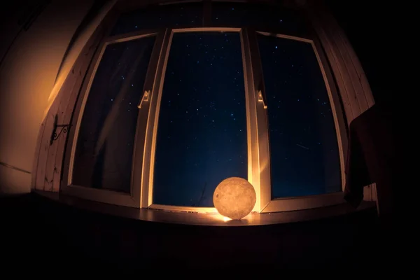 Night scene of stars seen through the window from dark room. Night sky inside dark room viewing from window with old vintage lantern. Long exposure shot