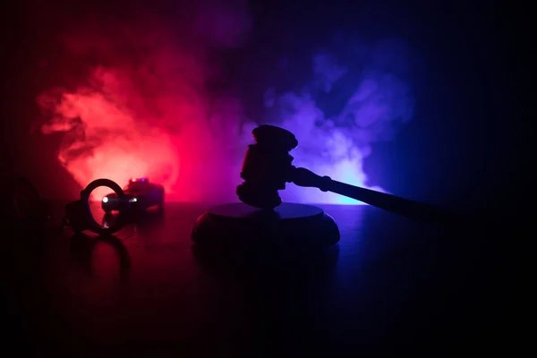 法律テーマは 正義の女神像の木製の机の上の裁判官のマレット 裏面に警察の車の手錠のシルエット 暗い霧の背景光と法律小槌 — ストック写真