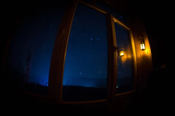 Night scene of stars seen through the window from dark room. Night sky inside dark room viewing from window with old vintage lantern. Long exposure shot