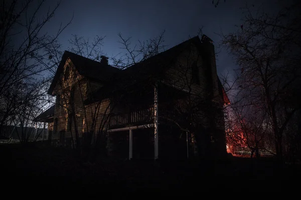 Old house with a Ghost in the forest at night or Abandoned Haunted Horror House in fog. Old mystic building in dead tree forest. Trees at night with moon. Surreal lights. Horror Halloween concept