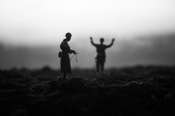 Battle scene. Military silhouettes fighting scene on war fog sky background. A German soldiers raised arms to surrender. Plastic toy soldiers with guns taking prisoner the enemy soldier. Artwork