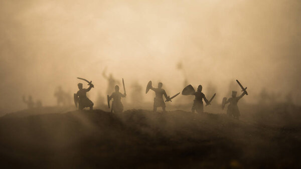 Medieval battle scene with cavalry and infantry. Silhouettes of figures as separate objects, fight between warriors on sunset foggy background. Selective focus