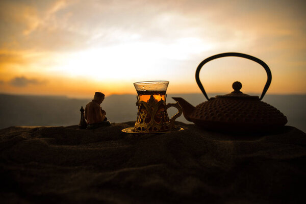 Arabic tea in traditional glass and pot on desert at sunset. Eastern tea concept. Artwork decoration on sand with tea. Selective focus