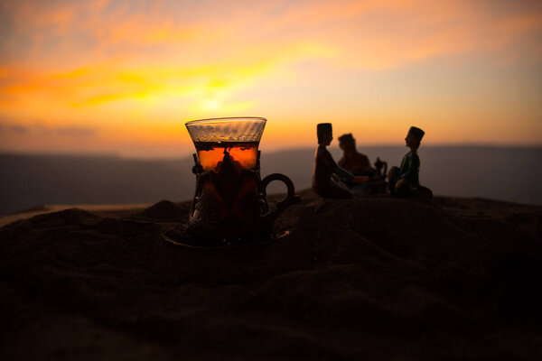 Arabic tea in traditional glass and pot on desert at sunset. Eastern tea concept. Artwork decoration on sand with tea. Selective focus