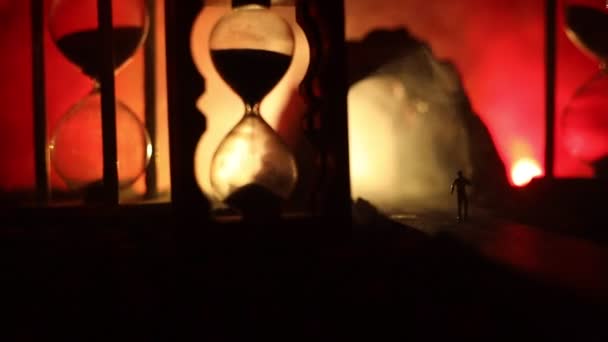 Time concept. Sand passing through the glass bulbs of an hourglass measuring the passing time as it counts down to a deadline. Silhouette of Hourglasses in smoke on dark background. With flowers — Stock Video