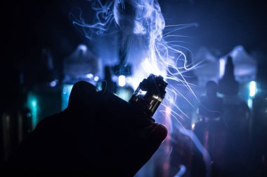 Vape kavramı. Elektronik sigara vape patlama. Duman bulutları ve vape sıvı şişe koyu arka plan üzerinde. Işık efektleri. Vape reklam olarak yararlı. Seçici odak
