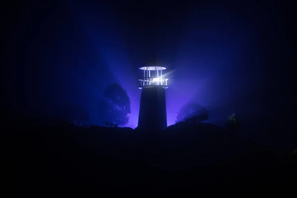 Phare avec faisceau lumineux la nuit avec brouillard. Vieux phare debout sur la montagne. Décoration de table. Fond tonique. Moonlighting . — Photo