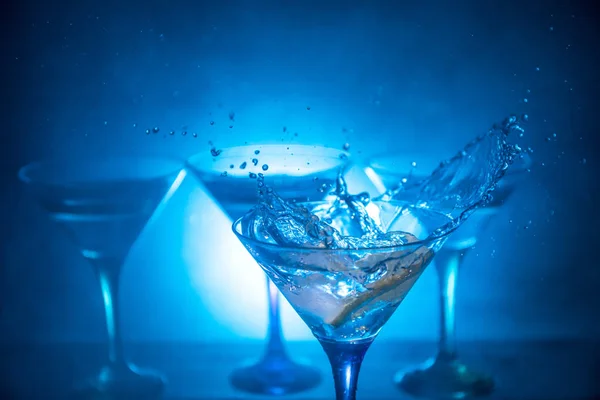 Martini cocktailglas girosaldi spatten op donker getinte rokerige achtergrond of een kleurrijke cocktail in glas met spatten en olijven. Partij club entertainment. Gemengd licht. Selectieve aandacht — Stockfoto