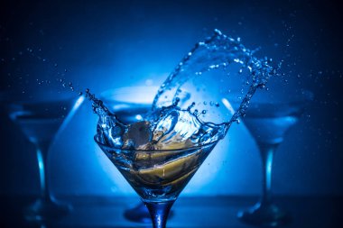 Martini kokteyl cam el koyu tonda dumanlı arka plan veya renkli kokteyl cam su sıçramalarına ve zeytin sıçramasına. Parti club eğlence. Karışık ışık. Seçici odak