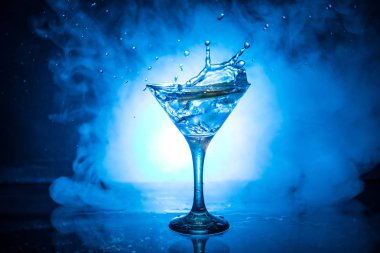 Martini kokteyl cam el koyu tonda dumanlı arka plan veya renkli kokteyl cam su sıçramalarına ve zeytin sıçramasına. Parti club eğlence. Karışık ışık. Seçici odak