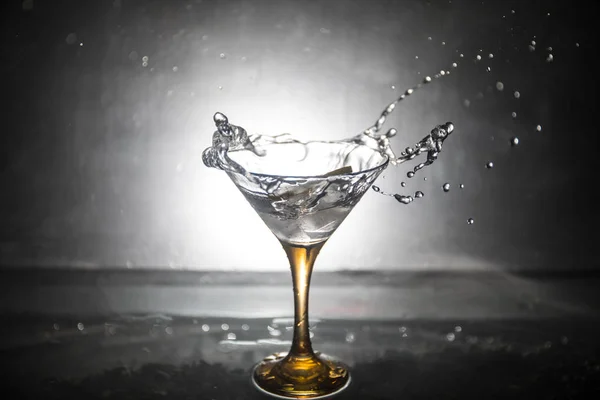 Martini cocktail glass in hand splashing on dark toned smoky background or colorful cocktail in glass with splashes and olives. Party club entertainment. Mixed light. Selective focus