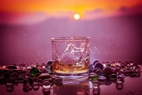 Een glas van whisky met ijs en goud zonlicht. Buiten schot van whisky met splash op zonsondergang achtergrond. — Stockfoto