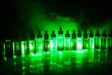 Vape kavramı. Duman bulutları ve vape sıvı şişe koyu arka plan üzerinde. Işık efektleri. Arka plan veya elektronik sigara reklam olarak kullanışlıdır. Seçici odak