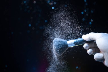 Makyaj, ışık ve duman ile koyu arka plan üzerinde kozmetik toz el fırça. Karanlık toz sıçrama. Seçici odak