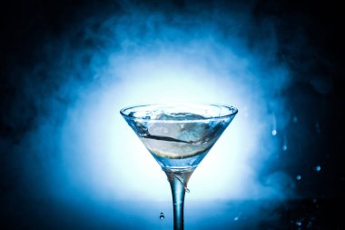 Martini kokteyl cam karanlık sıçramasına dumanlı arka plan veya renkli kokteyl cam su sıçramalarına ve limon ile tonda. Parti club eğlence. Karışık ışık. Seçici odak