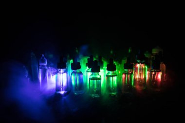 Vape kavramı. Duman bulutları ve vape sıvı şişe koyu arka plan üzerinde. Işık efektleri. Arka plan veya elektronik sigara reklam olarak kullanışlıdır. Seçici odak