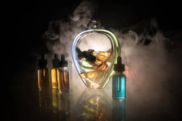 Vape concept. Smoke clouds and vape liquid bottles on dark background. Light effects. Useful as background or electronic cigarette advertisement. Selective focus