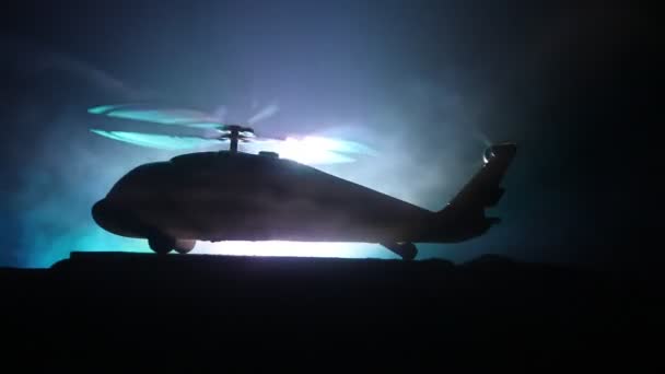 Silueta de helicóptero militar lista para volar desde zona de conflicto. Imágenes nocturnas decoradas con helicóptero comenzando en el desierto con niebla tonificada retroiluminada. Enfoque selectivo . — Vídeos de Stock