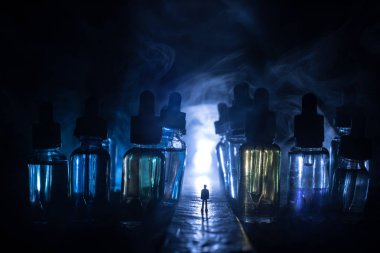 Vape kavramı. Sisli bir gecede dev cam şişe ile yolun ortasında duran bir adam silüeti elektronik sigara sıvı ile dolu. Işık arka plan üzerinde renkli sisli bulutlar.