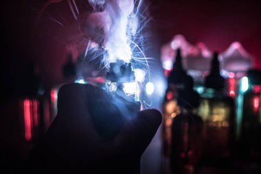 Vape kavramı. Elektronik sigara vape patlama. Duman bulutları ve vape sıvı şişe koyu arka plan üzerinde. Işık efektleri. Vape reklam olarak yararlı. Seçici odak