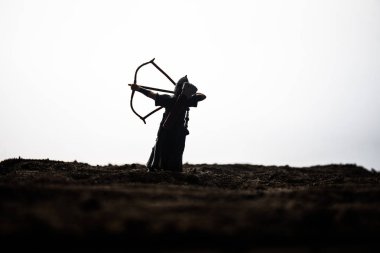 Geleneksel yay ile alan dizleri bükme archer ile ortaçağ savaş sahnesi. Koyu tonda sisli arka plan savaşçılar arasında siluetleri şekiller ayrı nesneler olarak mücadele. Akşam sahne.