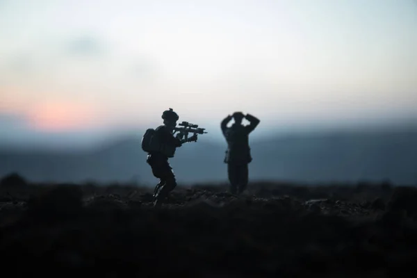 Battle scene. Military silhouettes fighting scene on war fog sky background. A German soldiers raised arms to surrender. Plastic toy soldiers with guns taking prisoner the enemy soldier. Artwork