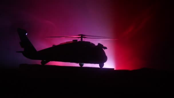 Silueta de helicóptero militar lista para volar desde zona de conflicto. Imágenes nocturnas decoradas con helicóptero comenzando en el desierto con niebla tonificada retroiluminada. Enfoque selectivo . — Vídeos de Stock