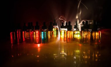 Vape kavramı. Duman bulutları ve vape sıvı şişe koyu arka plan üzerinde. Işık efektleri. Arka plan veya elektronik sigara reklam olarak kullanışlıdır. Seçici odak