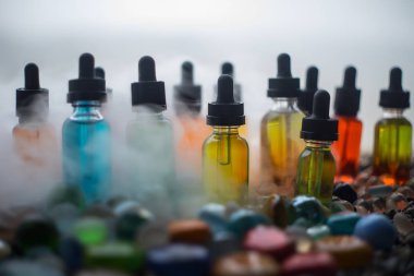 Vape kavramı. Güzel renkli vape sıvı cam şişeler taşlar hakkında açık. Arka plan veya elektronik sigara reklam olarak kullanışlıdır. Seçici odak