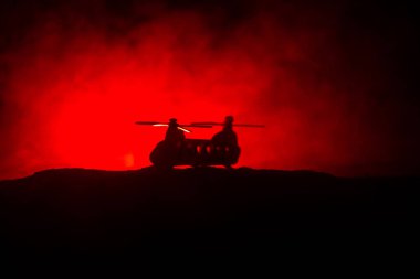 Askeri helikopterin silueti çatışma bölgesinden uçmaya hazır. Çölden başlayan sisli arka ışıklandırmalı helikopterle dekore edilmiş gece görüntüleri. Seçici odaklanma. Savaş konsepti