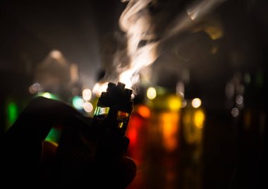 Vape kavramı. Elektronik sigara vape patlama. Duman bulutları ve vape sıvı şişe koyu arka plan üzerinde. Işık efektleri. Vape reklam olarak yararlı. Seçici odak