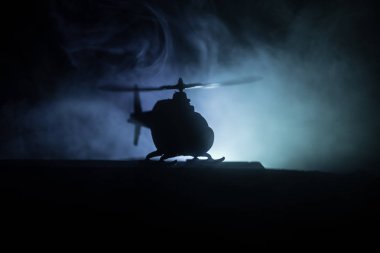 Askeri helikopterin silueti çatışma bölgesinden uçmaya hazır. Çölden başlayan sisli arka ışıklandırmalı helikopterle dekore edilmiş gece görüntüleri. Seçici odaklanma. Savaş konsepti