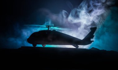 Askeri helikopterin silueti çatışma bölgesinden uçmaya hazır. Çölden başlayan sisli arka ışıklandırmalı helikopterle dekore edilmiş gece görüntüleri. Seçici odaklanma. Savaş konsepti