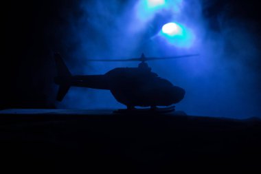 Askeri helikopterin silueti çatışma bölgesinden uçmaya hazır. Çölden başlayan sisli arka ışıklandırmalı helikopterle dekore edilmiş gece görüntüleri. Seçici odaklanma. Savaş konsepti