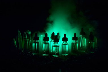 Vape kavramı. Duman bulutları ve vape sıvı şişe koyu arka plan üzerinde. Işık efektleri. Arka plan veya elektronik sigara reklam olarak kullanışlıdır. Seçici odak