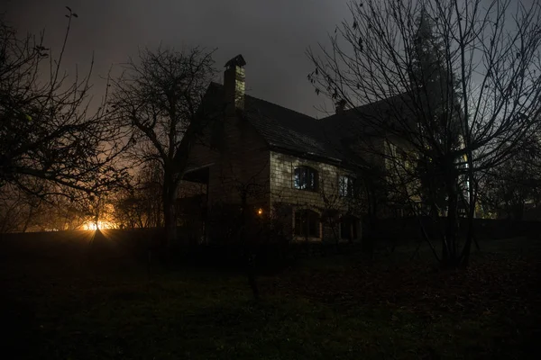 Old house with a Ghost in the forest at night or Abandoned Haunted Horror House in fog. Old mystic building in dead tree forest. Trees at night with moon. Surreal lights. Horror Halloween concept