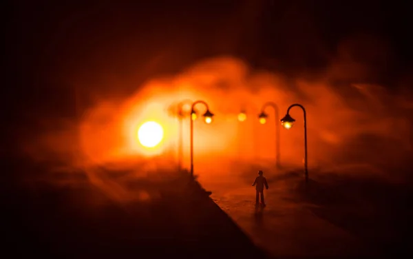 Artwork decoration. A man walking on road at night. The silhouette of a man standing in the middle of the road on a misty night. The glare of the street light against the fog sets a creepy mood.