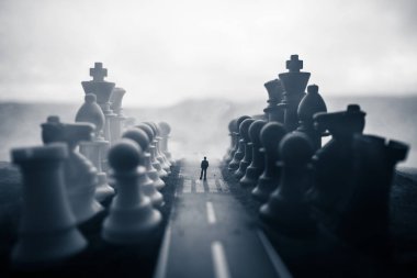 İş ve strateji fikirler satranç kavramı. Dev satranç figürleri ile yolun ortasında duran bir adam silüeti. Başarı ya da sorunları giden yolda küçük bir iş adamı. Resim dekorasyon