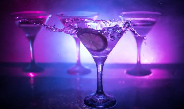 Martini kokteyl cam karanlık sıçramasına dumanlı arka plan veya renkli kokteyl cam su sıçramalarına ve limon ile tonda. Parti club eğlence. Karışık ışık. Seçici odak
