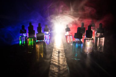 Vape kavramı. Sisli bir gecede dev cam şişe ile yolun ortasında duran bir adam silüeti elektronik sigara sıvı ile dolu. Işık arka plan üzerinde renkli sisli bulutlar.