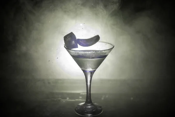 马提尼鸡尾酒玻璃溅在深色色调的烟熏背景或五颜六色的鸡尾酒在玻璃与飞溅和柠檬 派对俱乐部娱乐 混合光 选择性对焦 — 图库照片